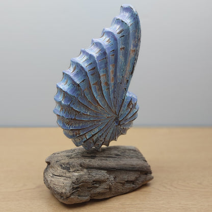 Decorative handmade blue shell sculpture on a wooden driftwood base against a plain background
