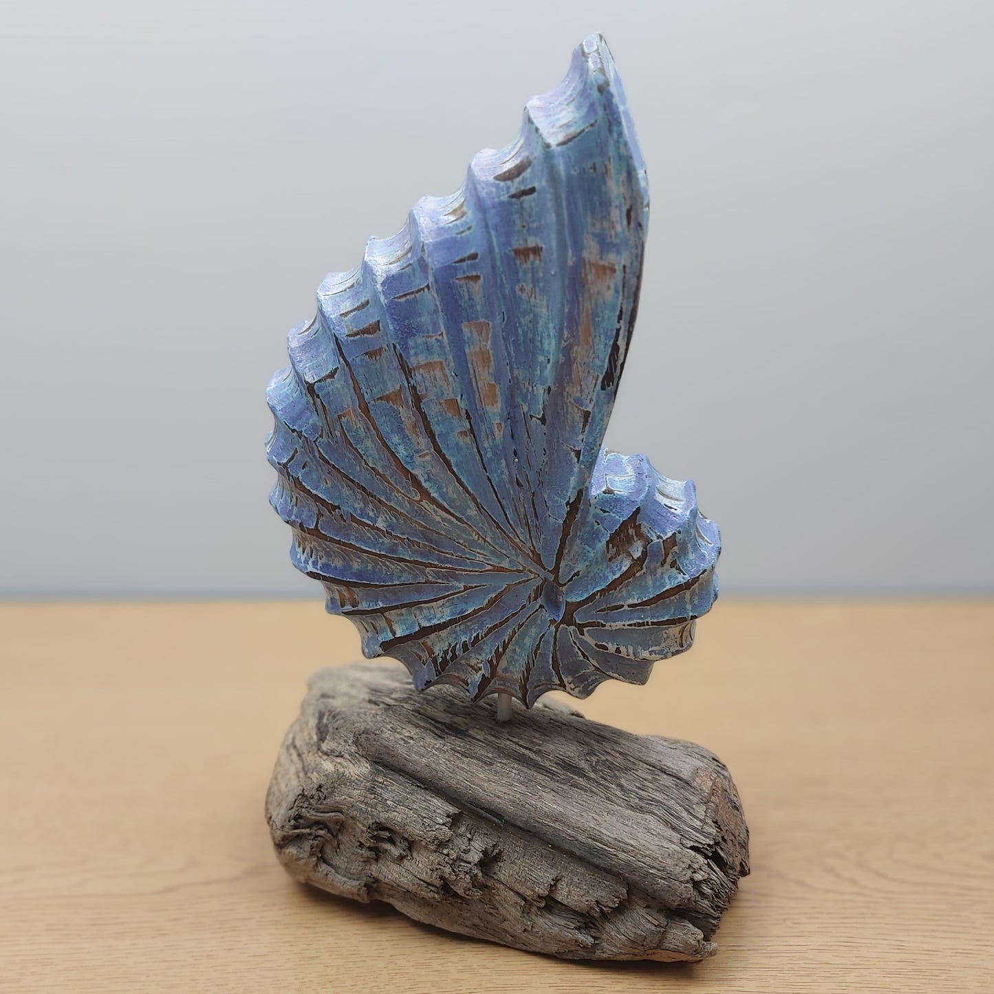 Decorative sculpture of a blue wooden shell on a wooden base against a plain background