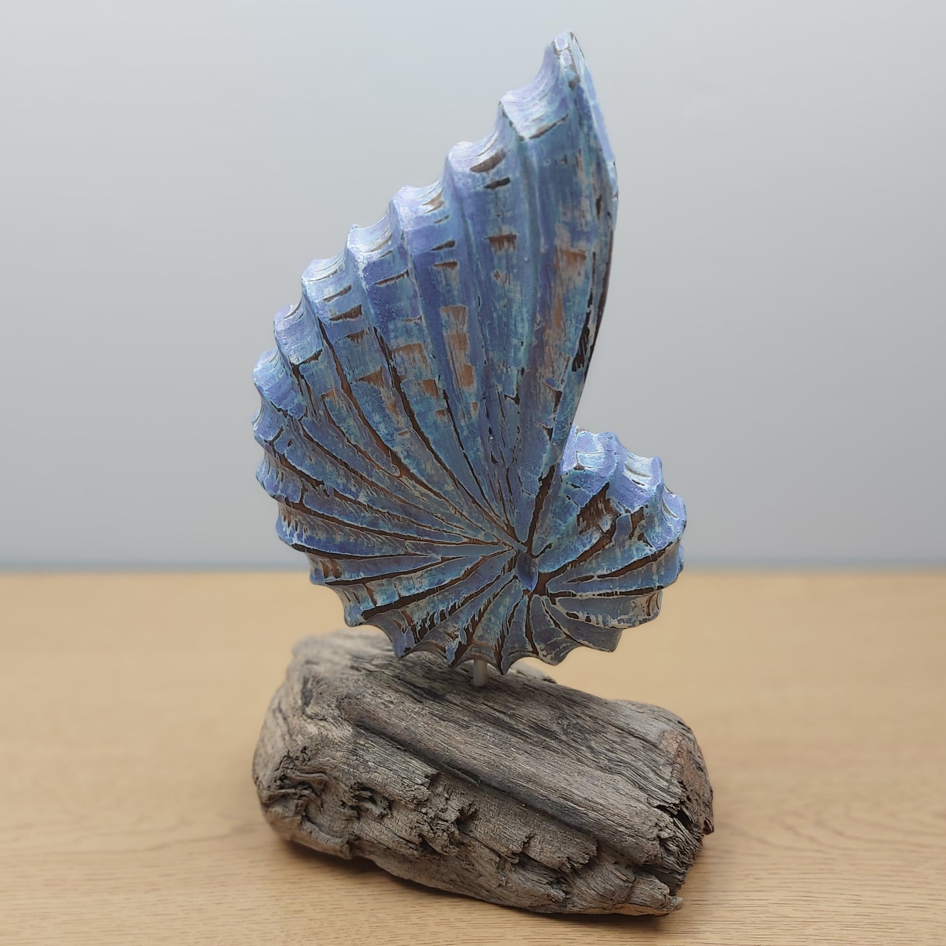 Decorative sculpture of a blue wooden shell on a wooden base against a plain background