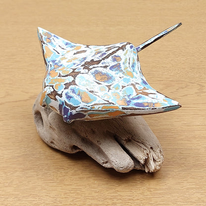 A hand made and painted Manta Ray Figurine, mounted on a driftwood base against a wooden background.