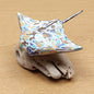 A hand made and painted Manta Ray Figurine, mounted on a driftwood base against a wooden background.