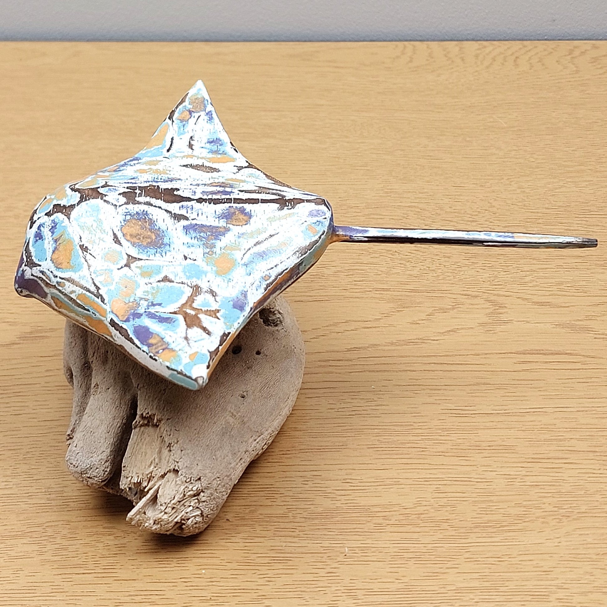 A sideview of a hand carved and painted wooden Manta Ray figurine with a colourful, abstract design on a wooden surface.