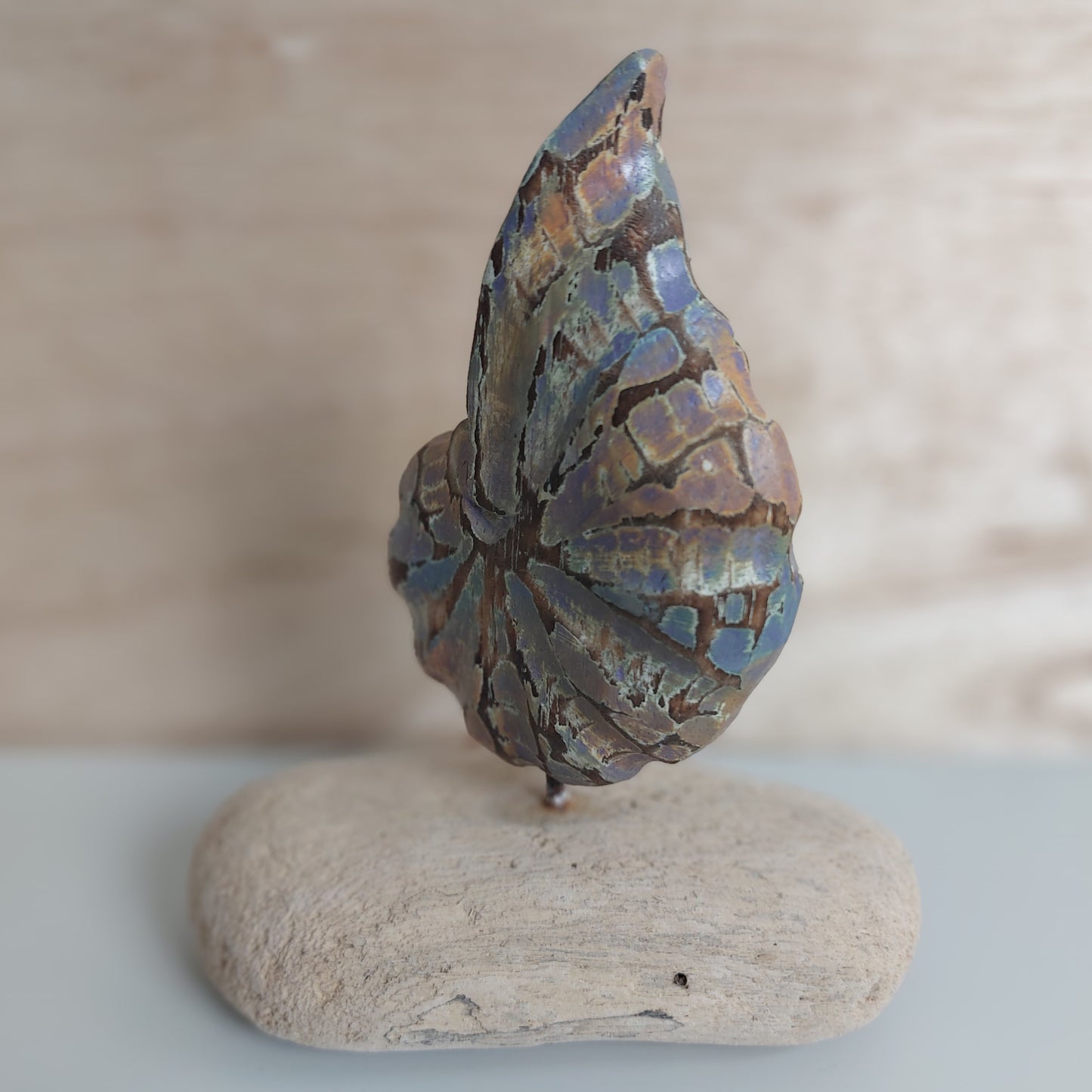 Decorative hand carved and painted wooden shell mounted on a piece of rustic wood on a beige background