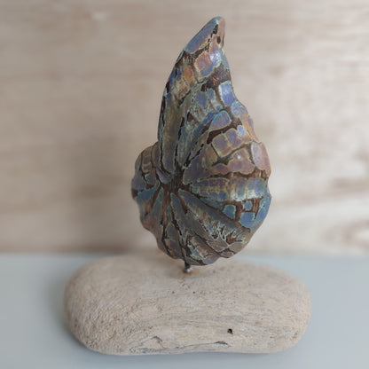 Decorative hand carved and painted wooden shell mounted on a piece of rustic wood on a beige background