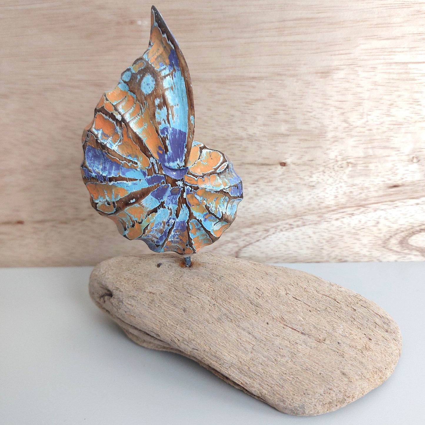 Hand carved and painted shell sculpture on a piece of driftwood with a wooden background