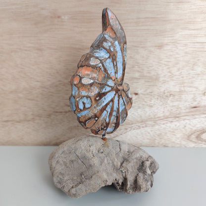 A hand carved and painted wooden shell made in Bali, mounted on a piece of dark brown driftwood against a pale background