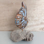 A hand carved and painted wooden shell made in Bali, mounted on a piece of dark brown driftwood against a pale background
