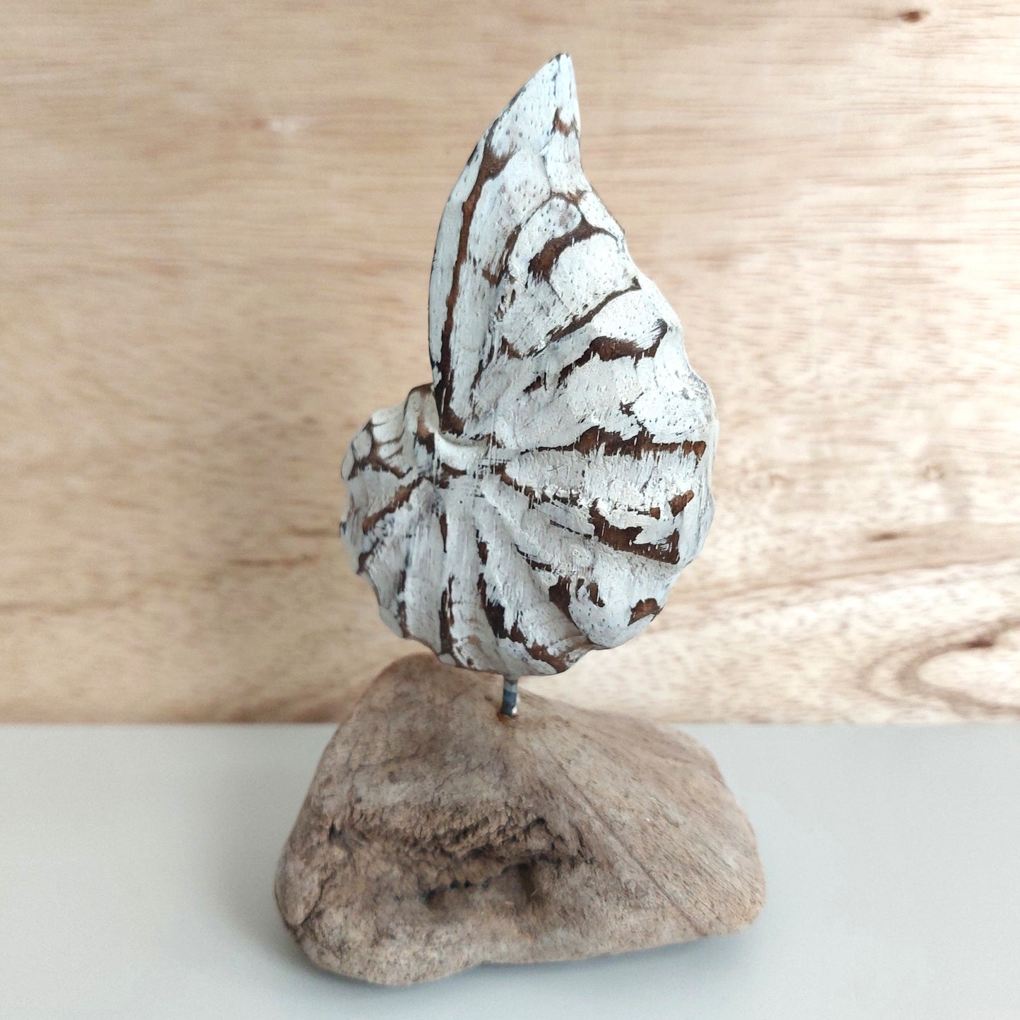 Decorative hand carved and painted white shell sculpture on a wooden base with a wooden background
