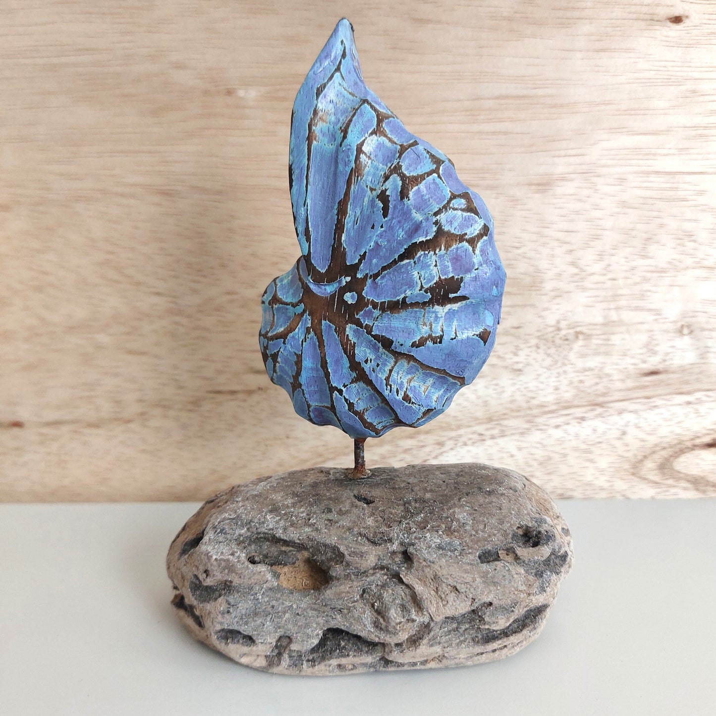 A handmade carved and painted blue wooden shell sculpture, mounted on a wooden base against a pale background.