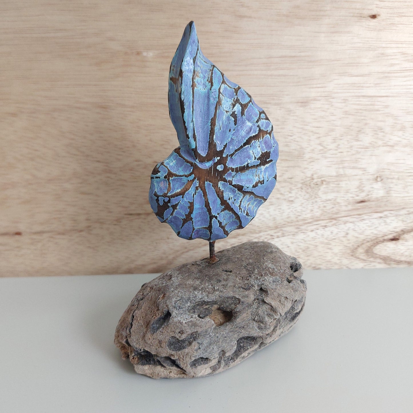 Decorative wooden shell sculpture with a blue and brown pattern mounted on a wooden base against a wooden background