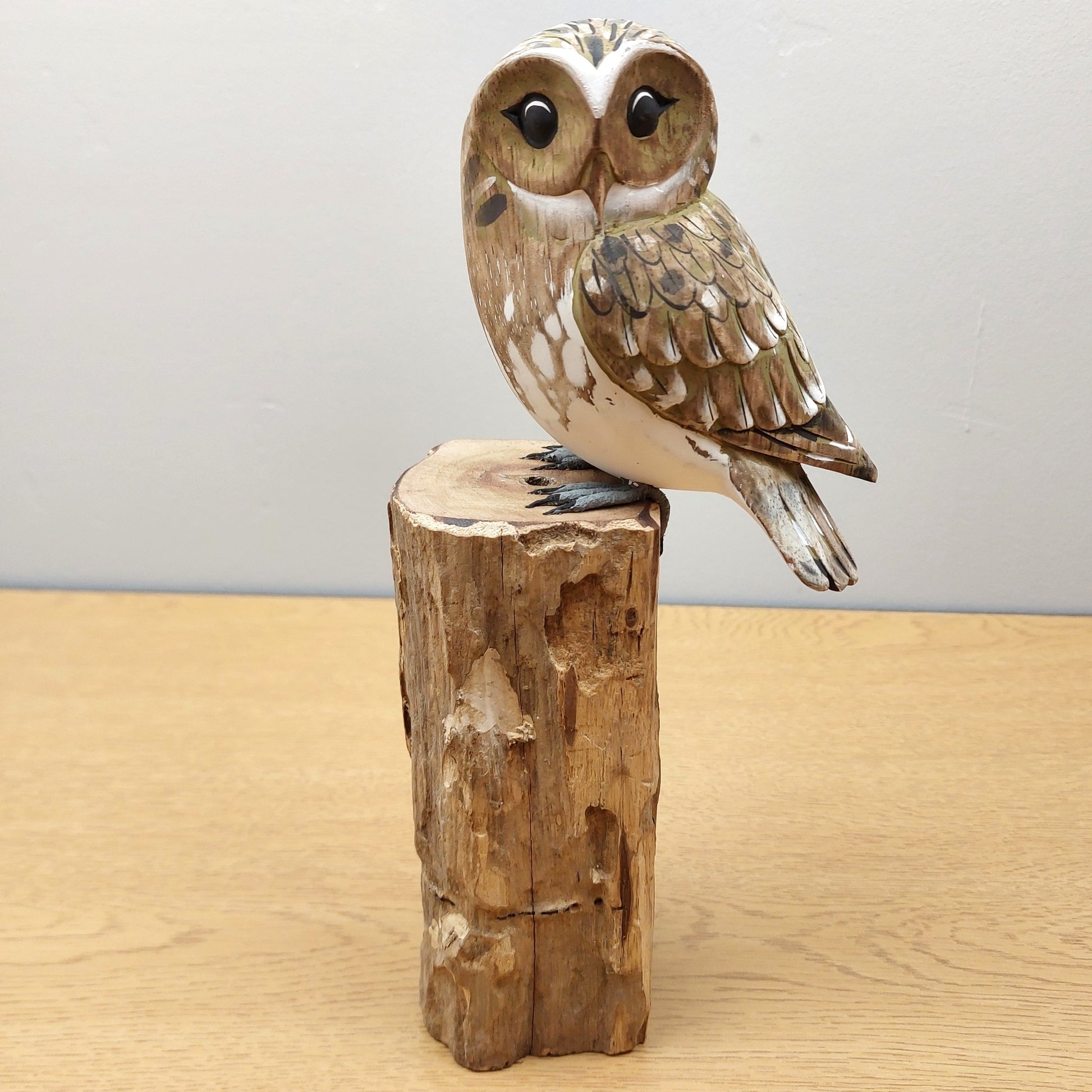 Handmade Carved Wooden brown owl figurine on a wooden stump against a plain background