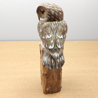 Wooden carved owl figurine looking away on a wooden base with a plain background