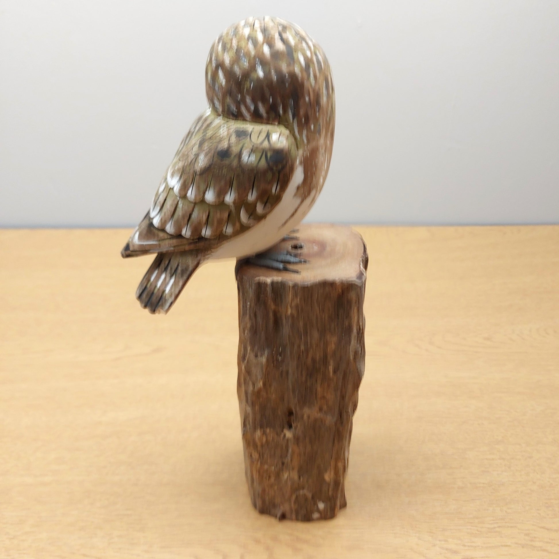 Wooden Handmade from Bali Carved owl figurine on a wooden log against a plain background