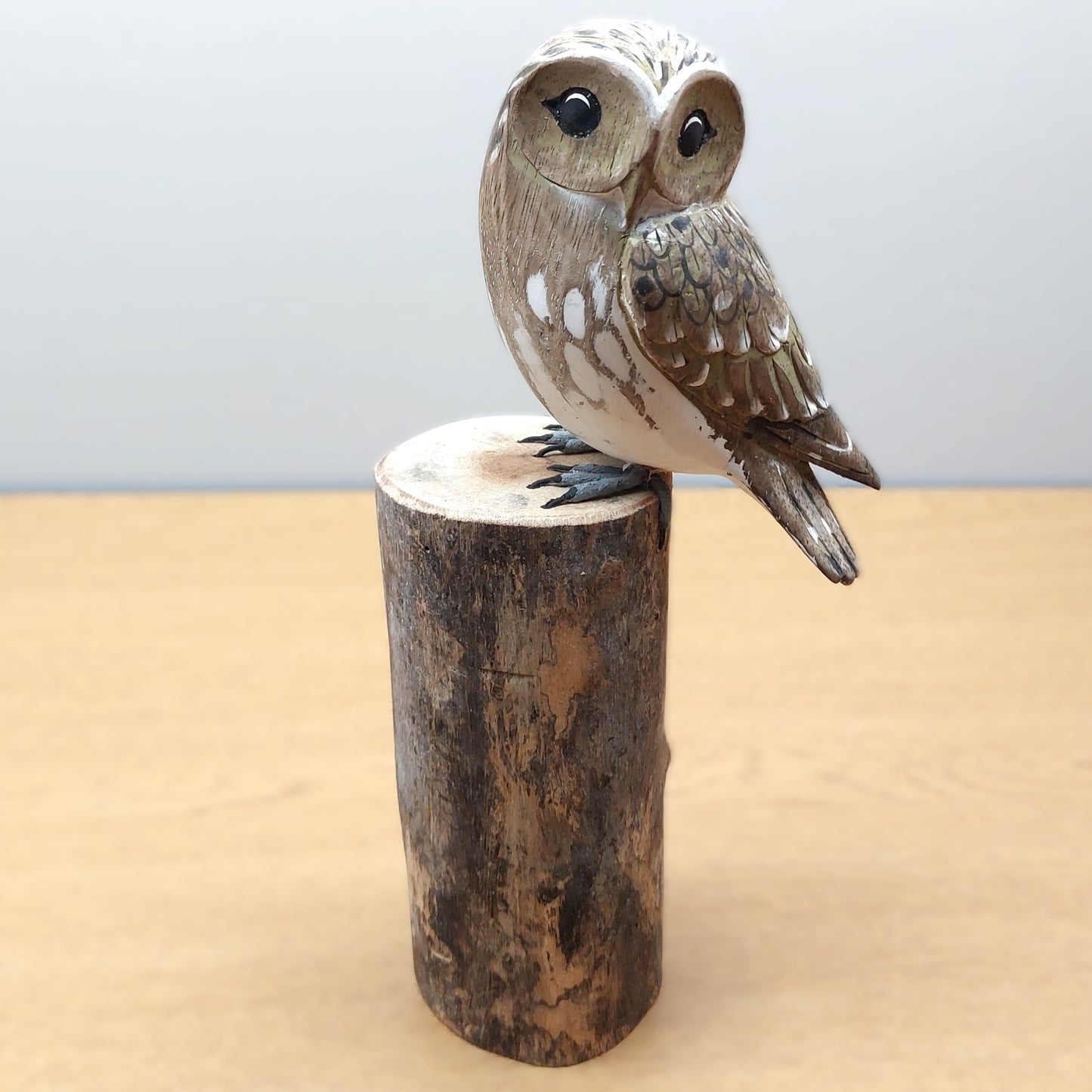 Wooden carved and painted owl figurine perched on a cylindrical wooden log base against a light background