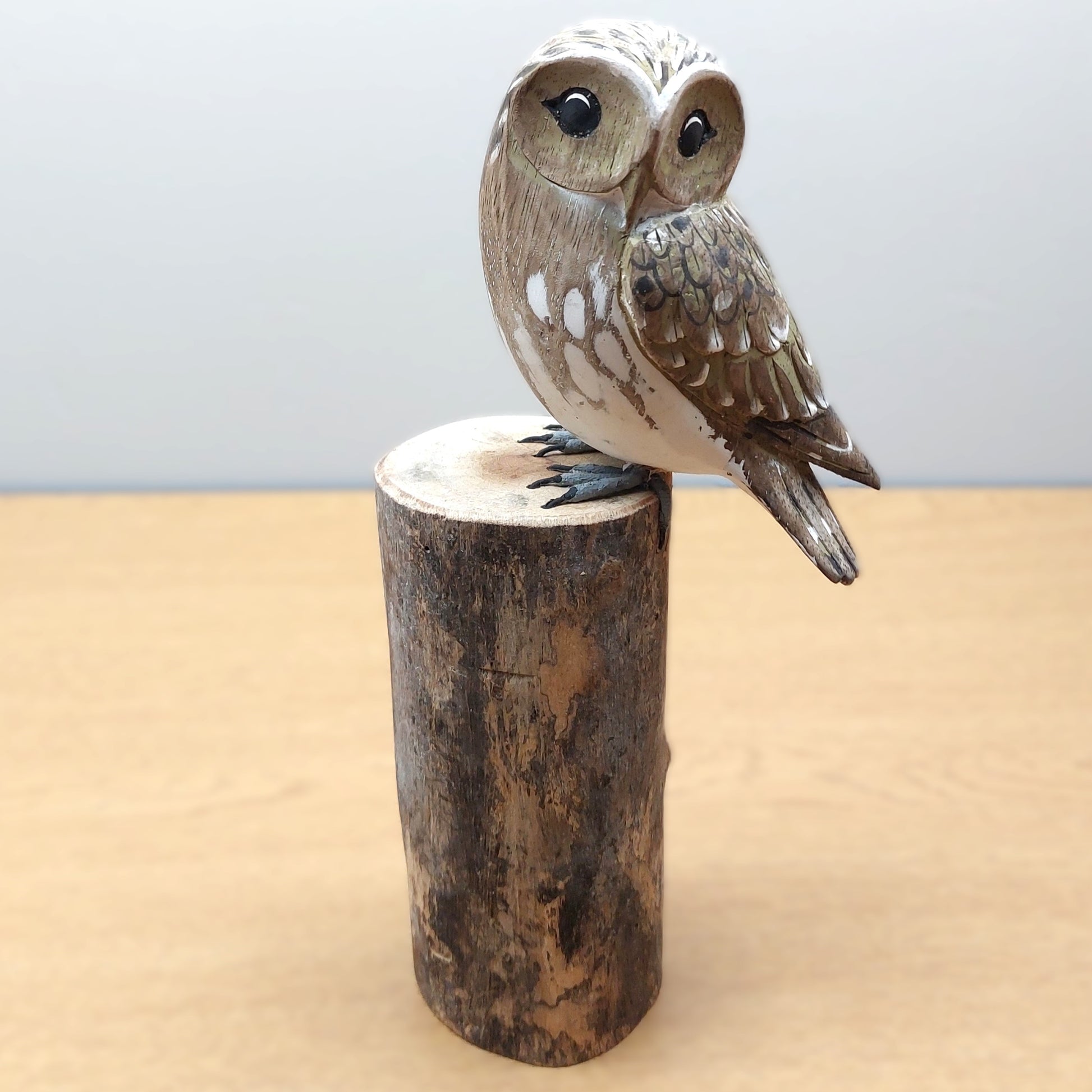 Wooden carved and painted owl figurine perched on a cylindrical wooden log base against a light background