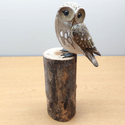 Wooden carved and painted owl figurine perched on a cylindrical wooden log base against a light background