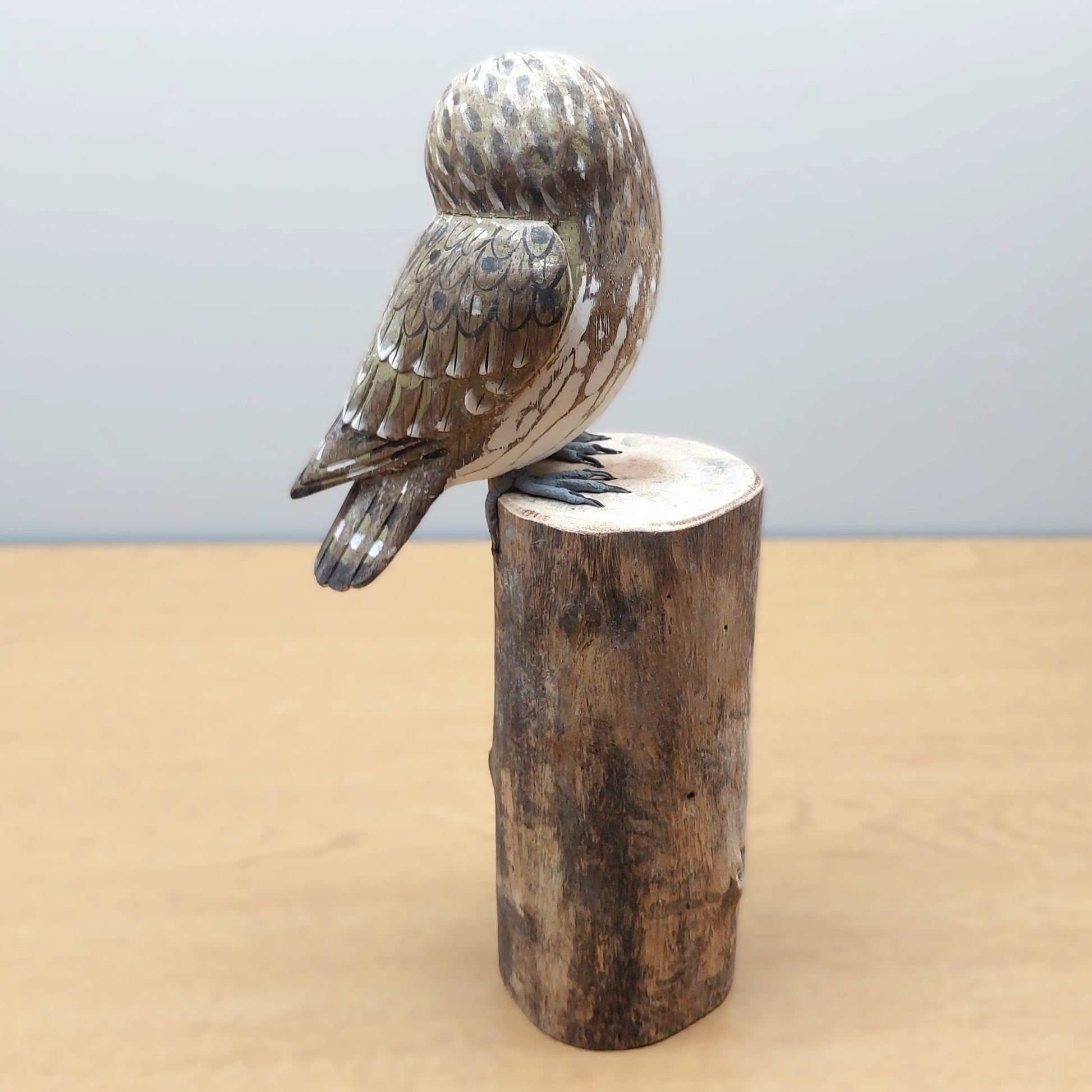 Hand carved and painted wooden owl sculpture on a wooden log from Bali against a light gray background