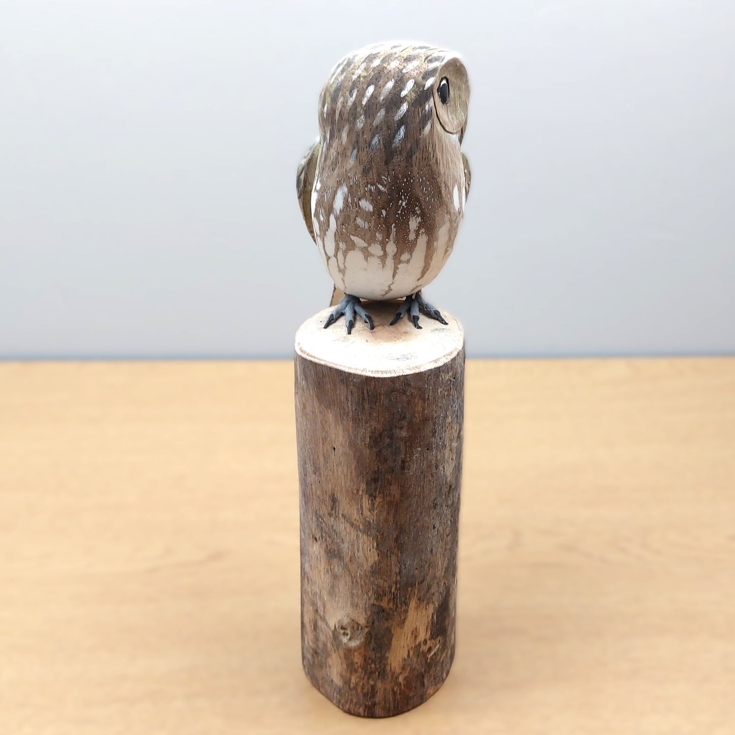 Decorative handmade and painted owl figurine on a wooden base against a light blue background