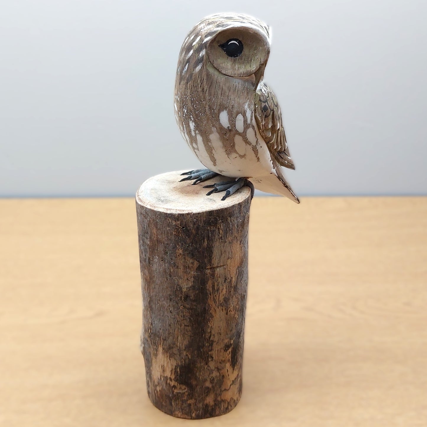 Wooden hand made and painted ornate owl figurine perched on a cylindrical wooden log against a light background