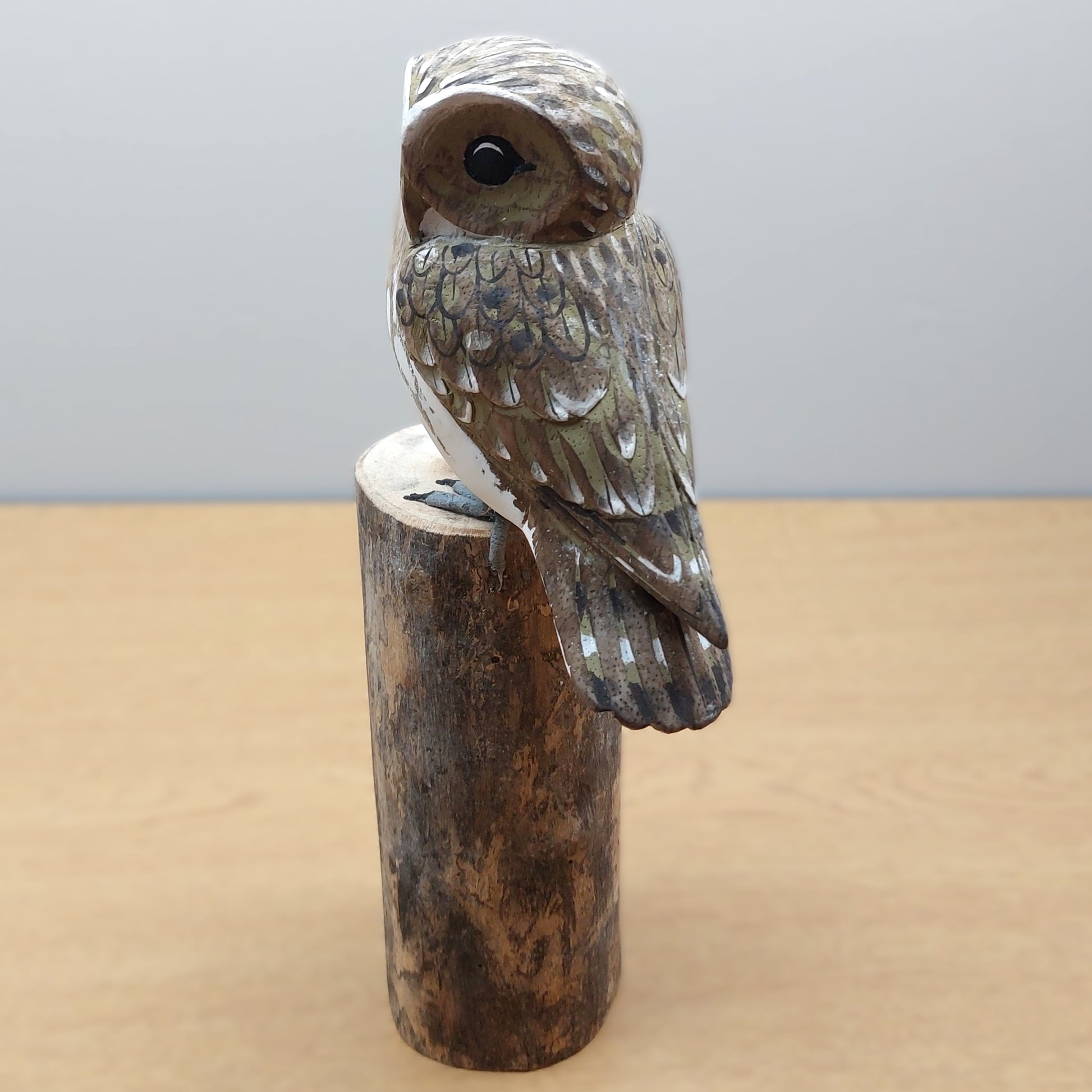 Wooden owl figurine made in Bali on a wooden log against a gray background