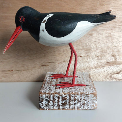 Hand carved Wooden Model of an Oystercatcher bird with a red beak and legs on a wooden block against a wooden background