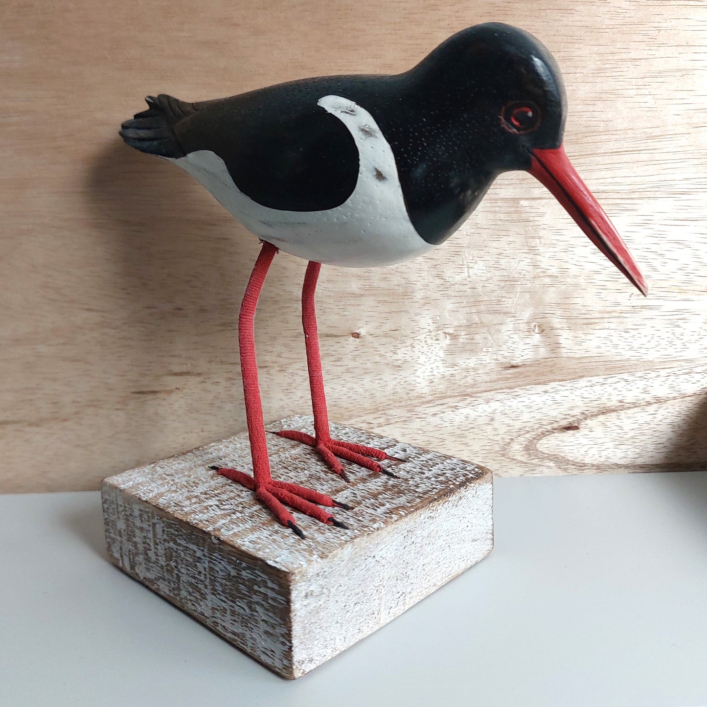 Wooden Hand carved and painted Oystercatcher bird figurine on a wooden block with a light wood background
