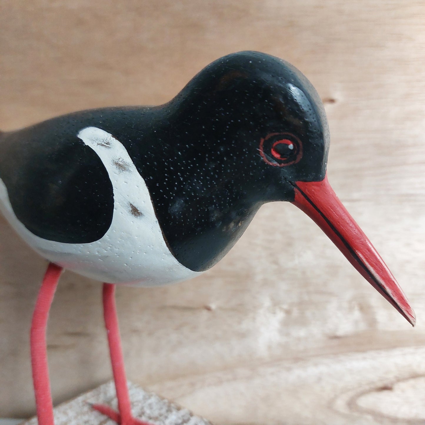 Close-up of a hand carved and painted black and white Oystercatcher figurine with a red beak on a wooden background