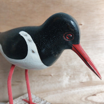 Close-up of a hand carved and painted black and white Oystercatcher figurine with a red beak on a wooden background