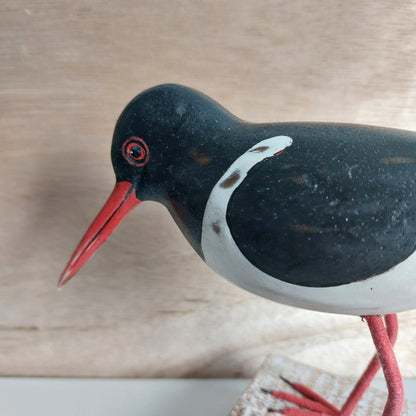 Close-up of a decorative Oystercatcher bird ornament with a red beak on a wooden surface