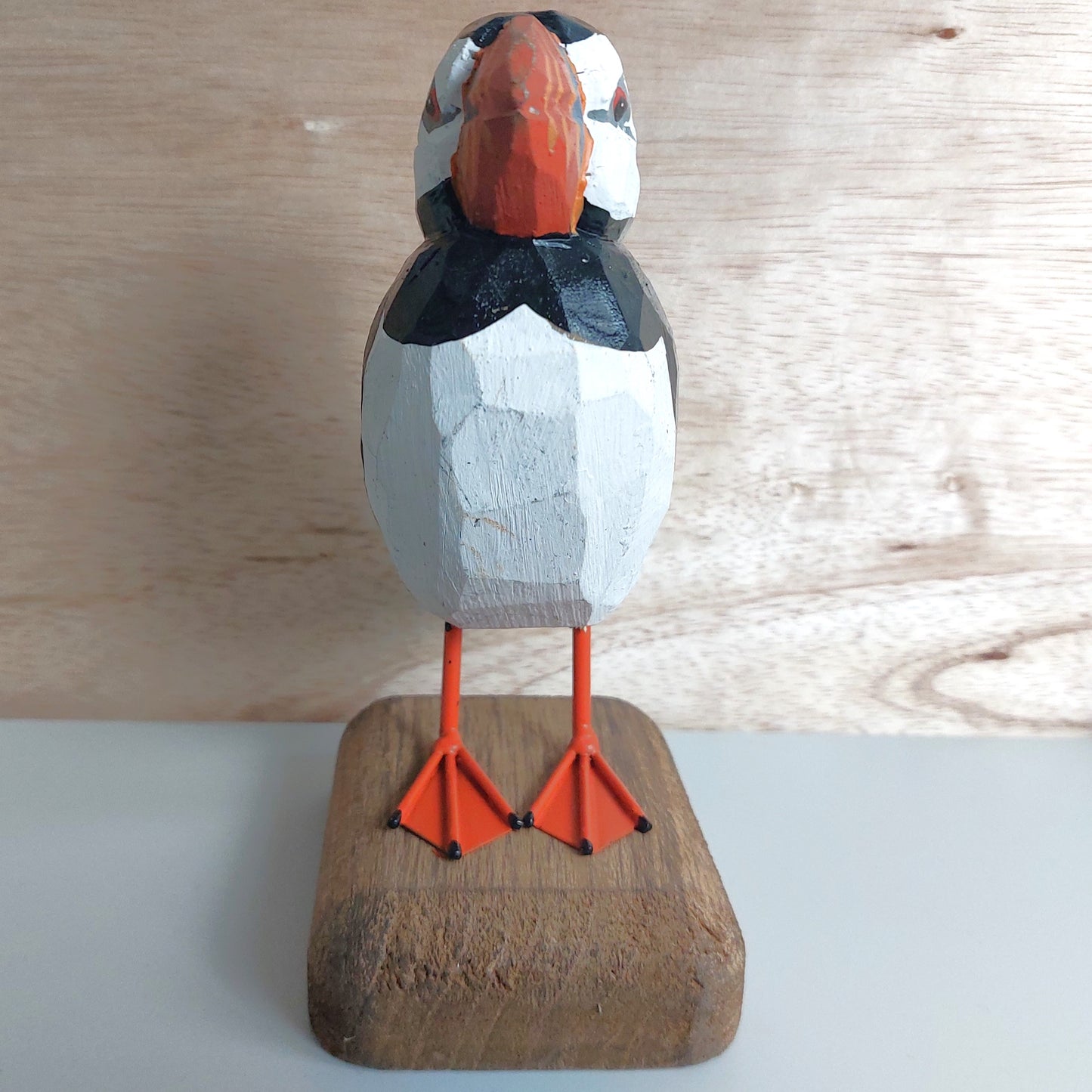 Wooden puffin figurine on a wooden base against a light wood panel background
