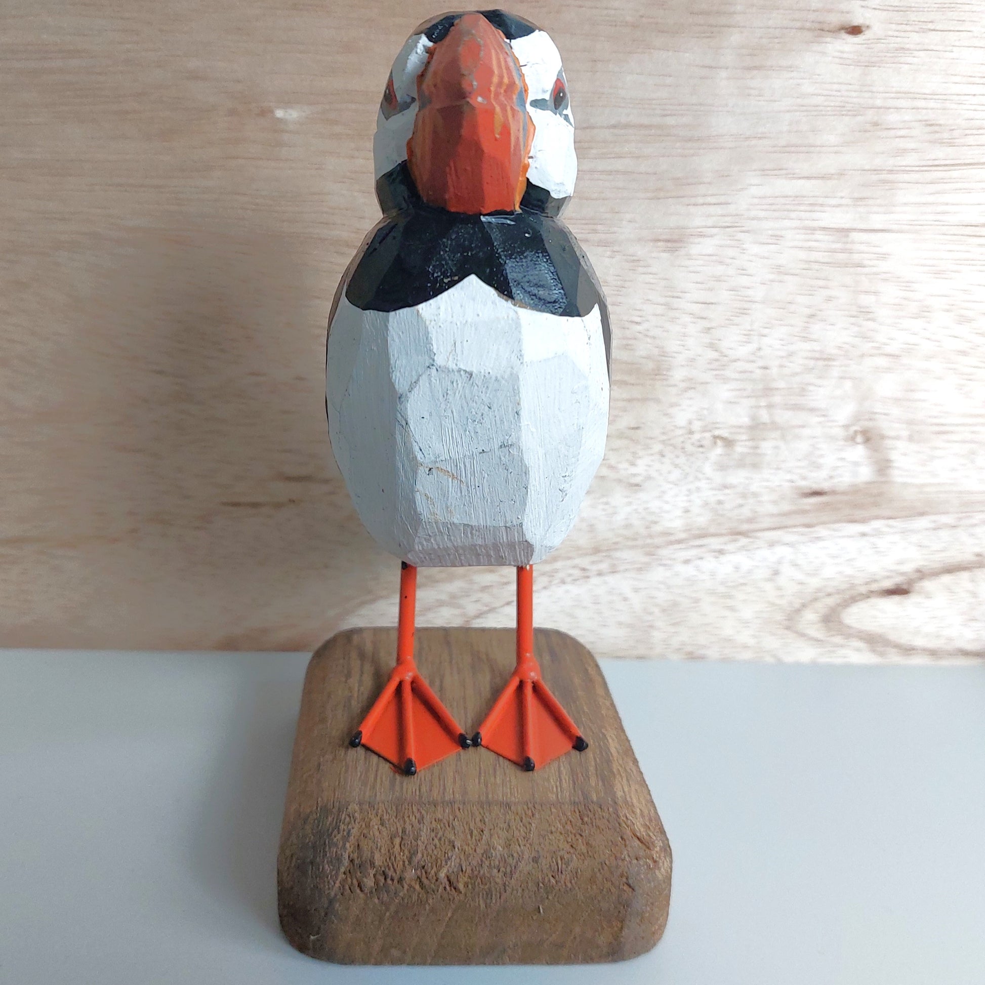 Wooden puffin figurine on a wooden base against a light wood panel background