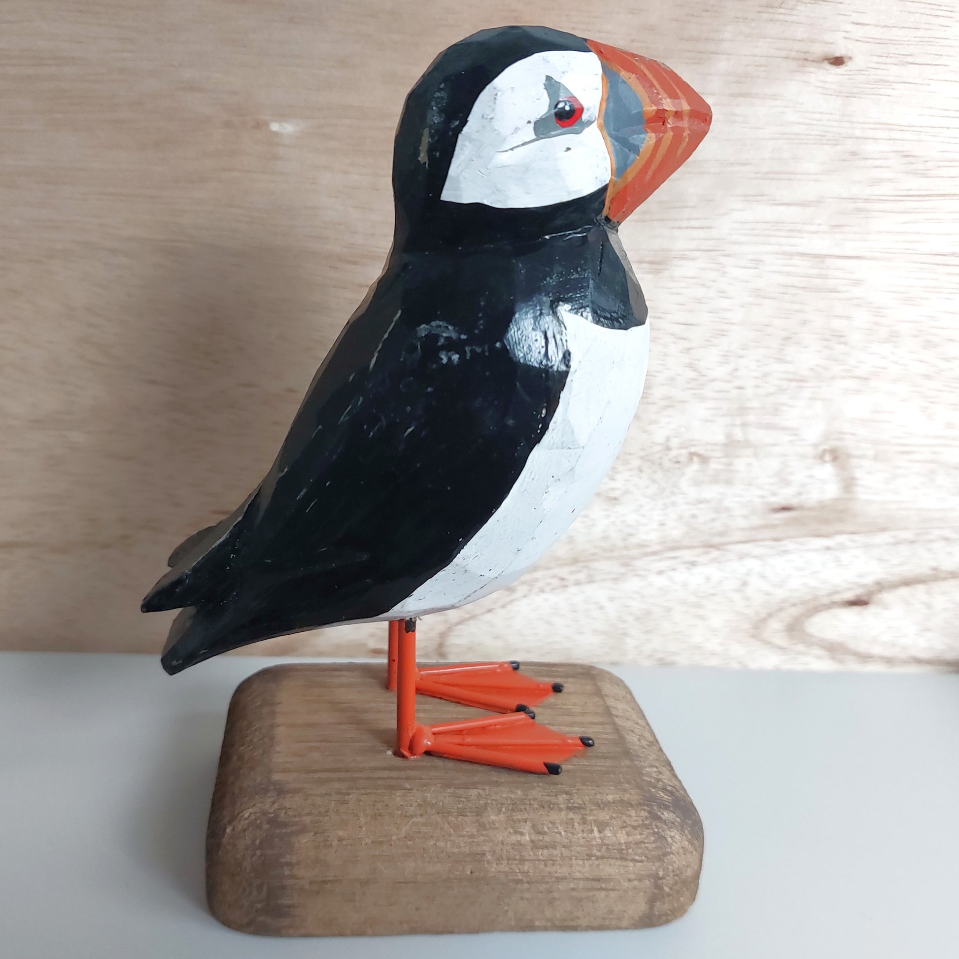 Wooden puffin figurine on a wooden base against a light wood panel background