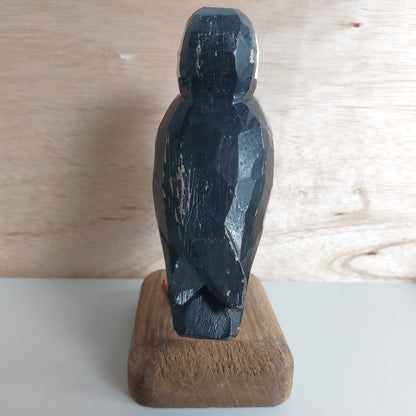 Black wooden puffin sculpture on a wooden base against a light wood panel background