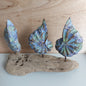 Three blue, green and brown hand carved wooden shells attached to a piece of driftwood on a wooden surface.