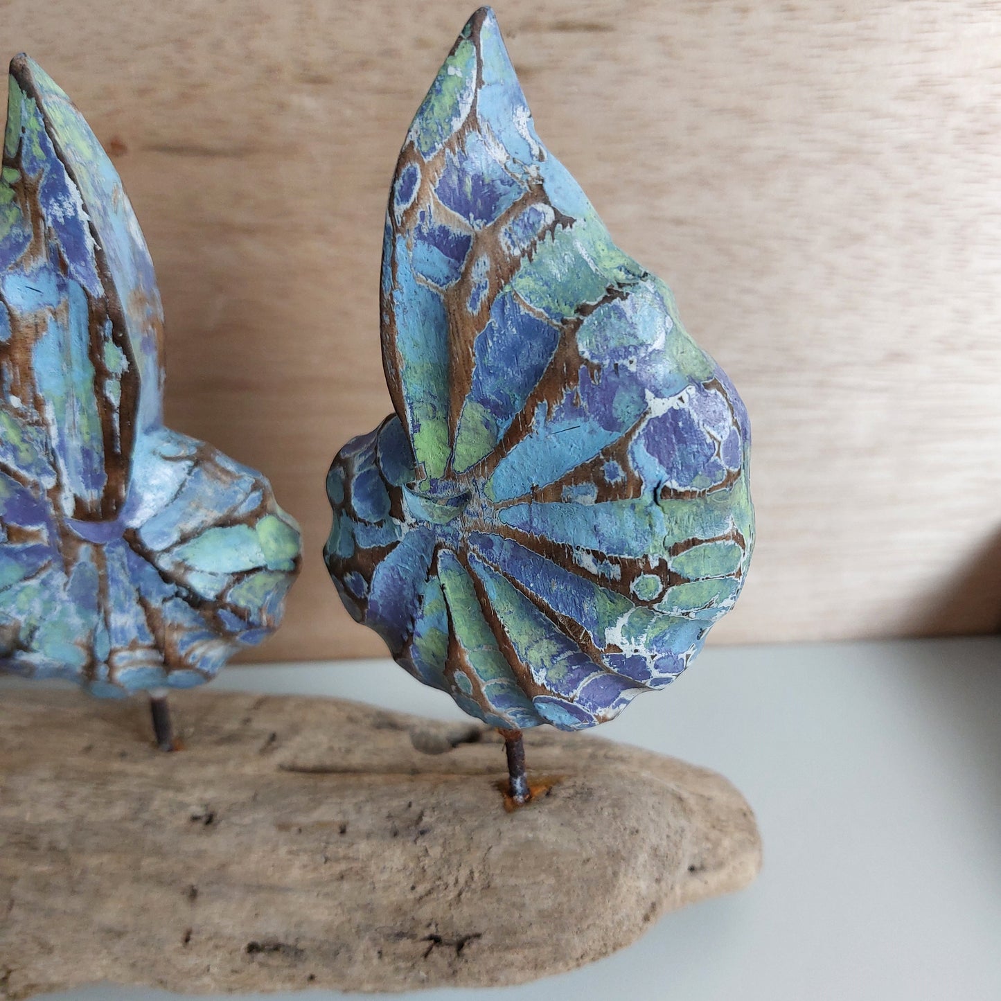 Close up of a hand painted and carved wooden shell mounted on a driftwood base with a neutral background.