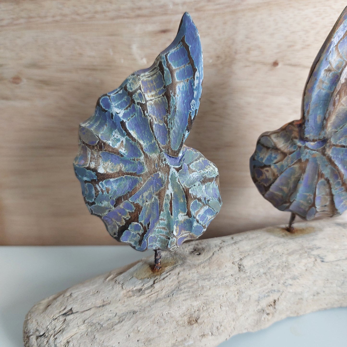 Blue and brown carved and painted wooden shells mounted on a reclaimed driftwood base against a wooden background.