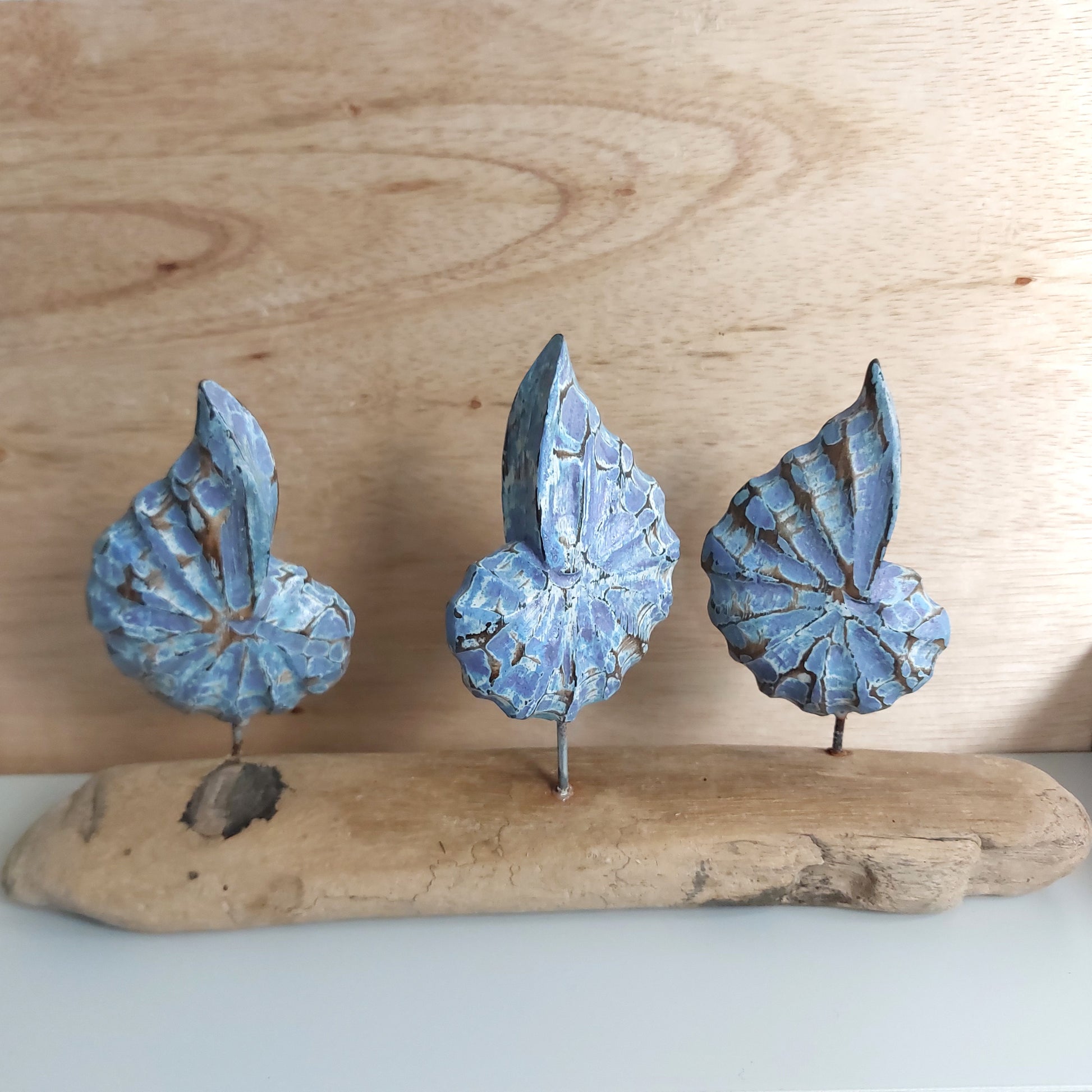Three wooden hand carved and painted blue and brown shell sculptures on a piece of driftwood against a wooden background