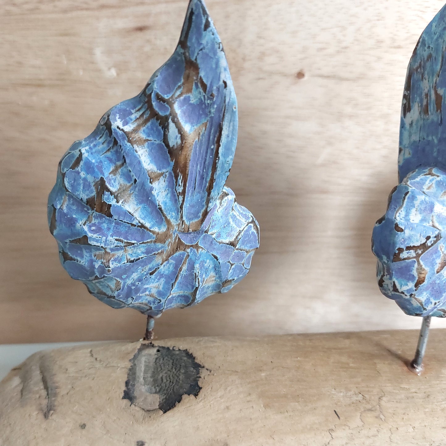 A close up of a wooden blue and brown shell figurine mounted on a piece of driftwood on a wooden surface
