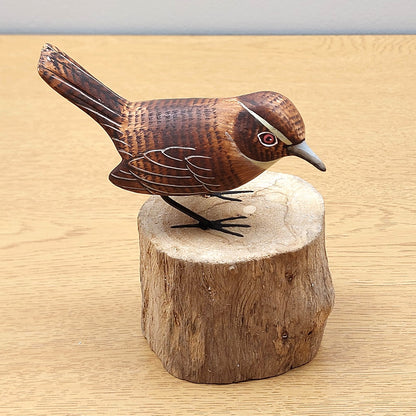 Wooden handmade carved Wren bird figurine on a wooden log base against a beige background