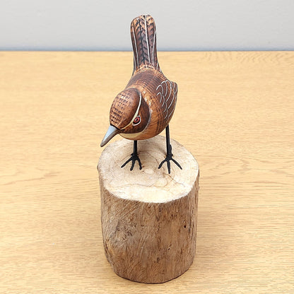 Wooden Wren bird figurine on a wooden block against a light gray background