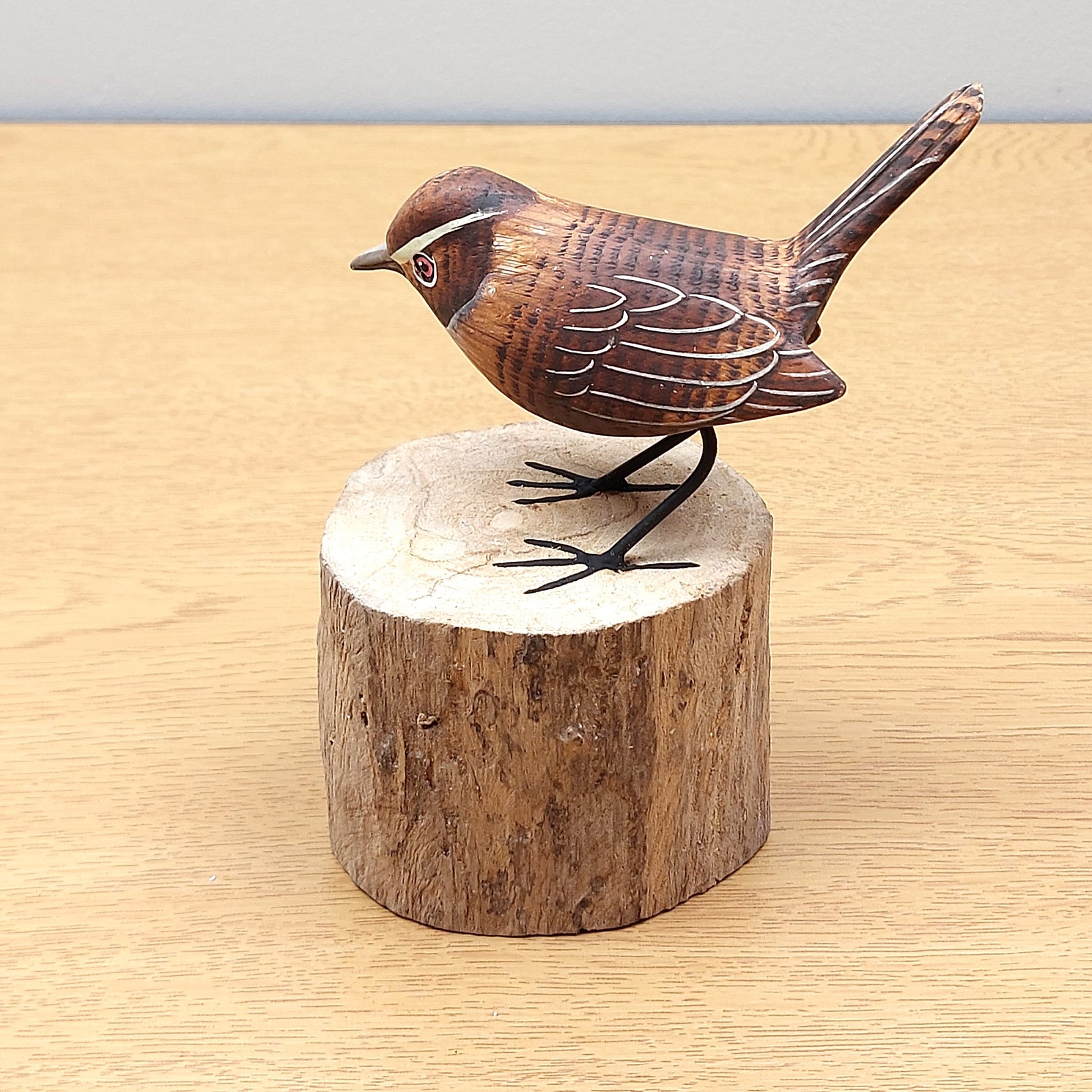 Wooden hand carved Wren bird figurine on a wooden log base against a light background