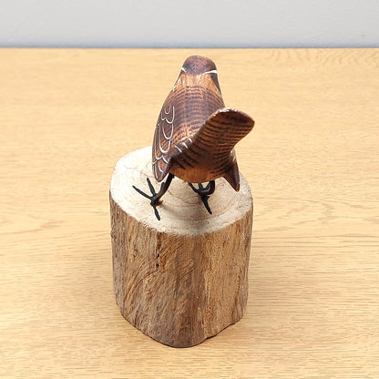 Wooden Handmade and painted Wren bird figurine on a wooden log block against a beige background.