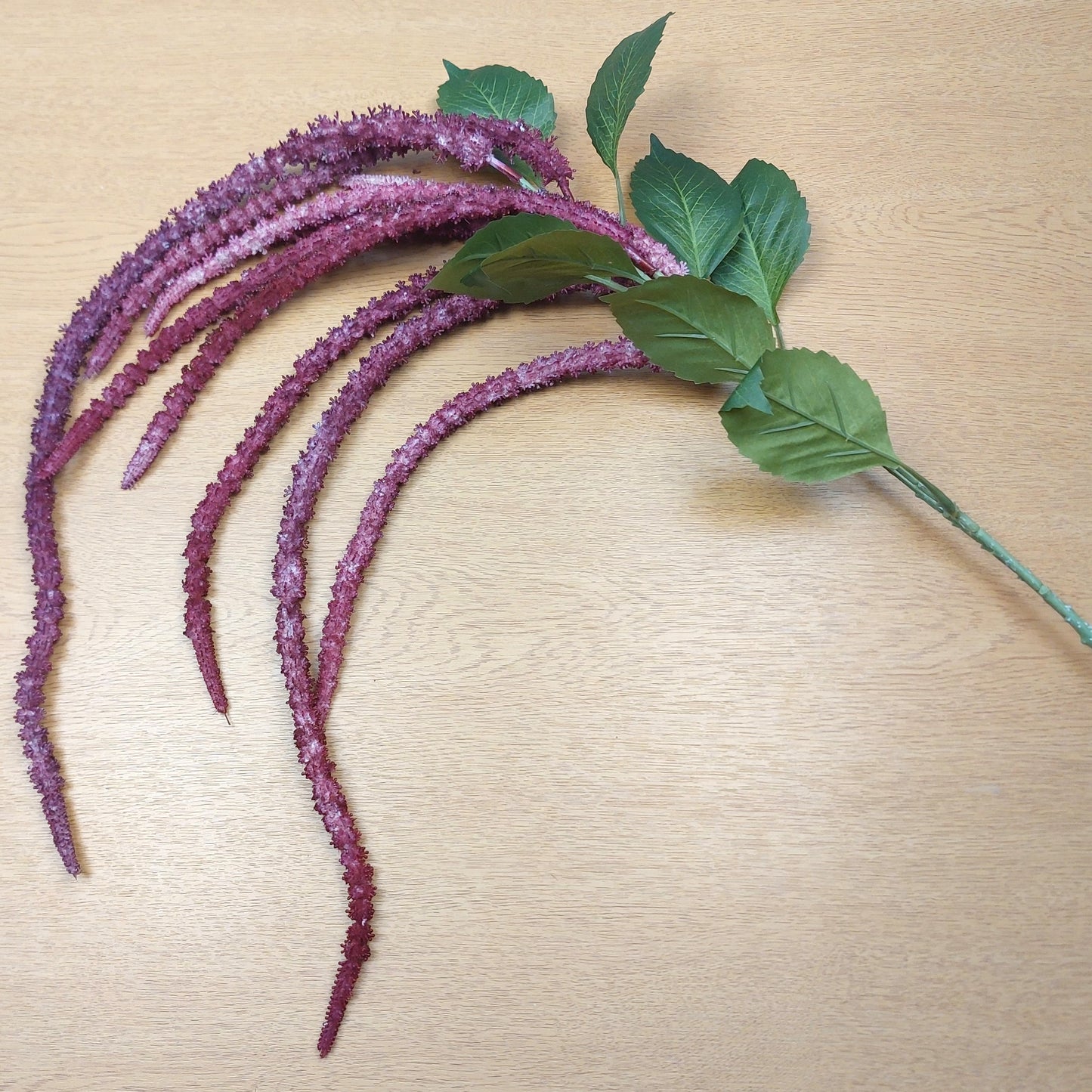 Purple artificial amaranthus flower stems with green leaves on a beige surface