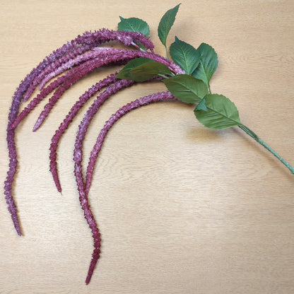 Purple artificial amaranthus flower stems with green leaves on a beige surface