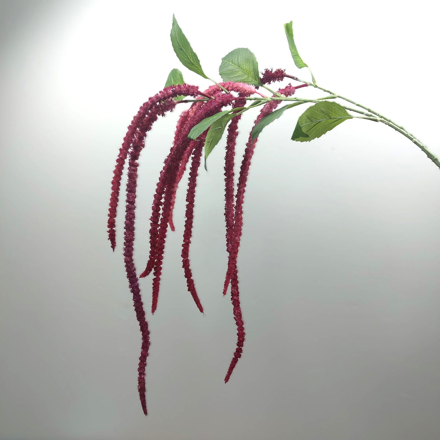 Purple flower artificial amaranthus branch with green leaves on a light gray background